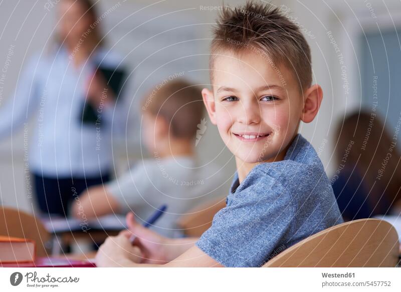 Porträt eines lächelnden Schuljungen in der Klasse Schüler Schule Portrait Schulklasse smart Stift Schulheft Unterrichtsstunde Schreibtisch optimistisch Wissen