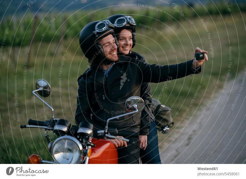 Porträt eines glücklichen jungen Paares auf einem Oldtimer-Motorrad, das ein Selfie am Straßenrand macht Transport Transportwesen KFZ Verkehrsmittel Motorräder