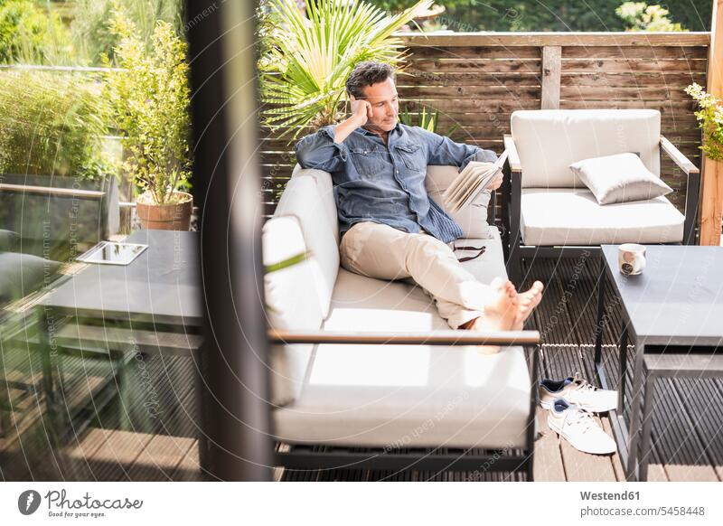Selbstbewusster Mann entspannt sich auf der Terrasse, liest Buch Bücher Couch Couches Liege Sofas Lektüre sitzend sitzt Muße konzentrieren konzentriert