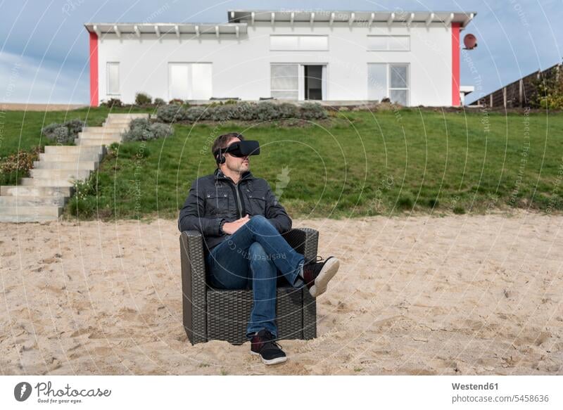 Mann sitzt im Sessel am Strand und trägt eine VR-Brille Virtuelle Realität Virtuelle Realitaet Männer männlich Beach Straende Strände Beaches Brillen sitzen