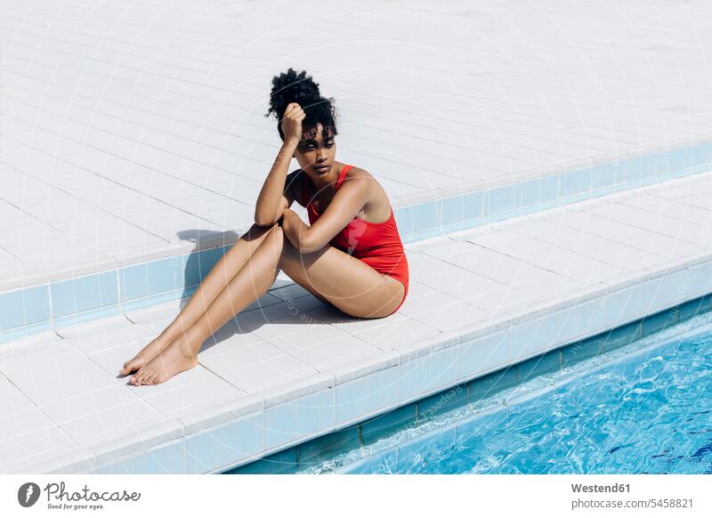 Porträt einer nachdenklichen jungen Frau in rotem Badeanzug am Poolufer sitzend Badebekleidung Badeanzuege Badeanzüge entspannen relaxen sitzt Jahreszeiten