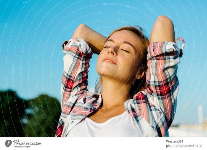 Frau mit geschlossenen Augen und Händen hinter dem Kopf gegen den klaren Himmel stehend Farbaufnahme Farbe Farbfoto Farbphoto Außenaufnahme außen draußen