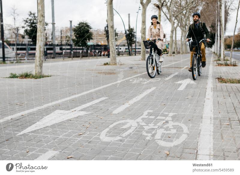 Pärchen fährt mit E-Bikes in der Stadt auf dem Fahrradweg radfahren fahrradfahren radeln staedtisch städtisch Radweg Paar Paare Partnerschaft Fahrräder Räder