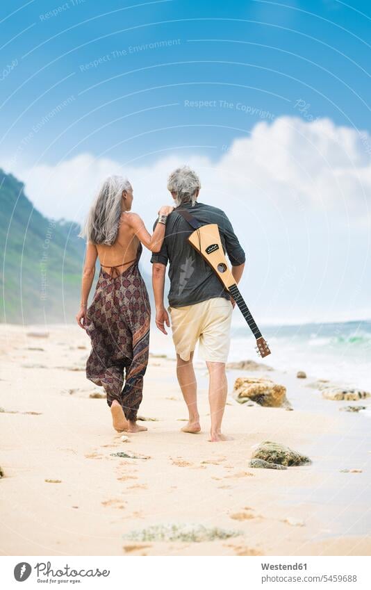 Rückenansicht von älteren Hippie-Paar mit Gitarre schlendern nebeneinander am Strand Hippies Flower power Blumenkinder Beach Straende Strände Beaches
