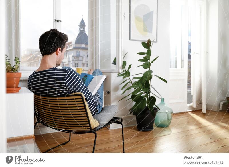 Mann sitzt zu Hause und benutzt Laptop Sessel arbeiten Arbeit Stuhl Stuehle Stühle Wohnen Verbindung verbunden verbinden Anschluss Notebook Laptops Notebooks