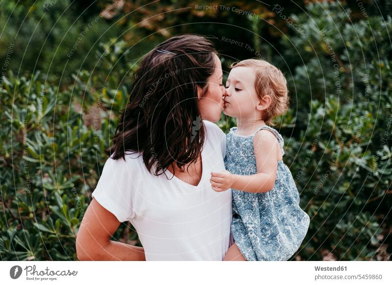Glückliche Mutter und Tochter küssen sich im Park stehend und küssen sich Farbaufnahme Farbe Farbfoto Farbphoto Außenaufnahme außen draußen im Freien Tag