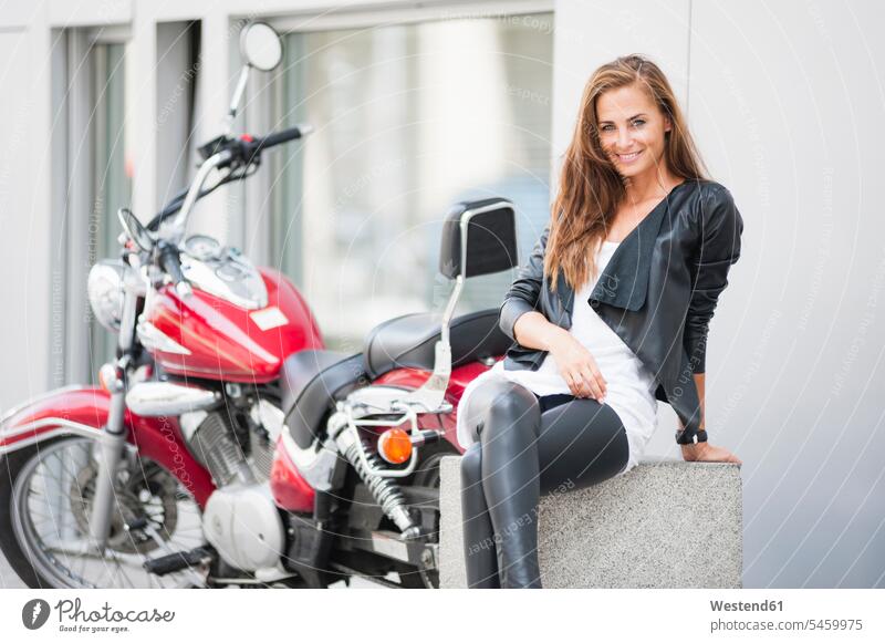 Porträt einer lächelnden Frau, die in der Stadt vor einem Motorrad sitzt KFZ Verkehrsmittel Motorräder sitzend freuen Glück glücklich sein glücklichsein Muße