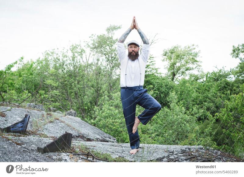 Bärtiger Mann mit Mütze, der Baumhaltung auf Felsen gegen Bäume übt Farbaufnahme Farbe Farbfoto Farbphoto Österreich Außenaufnahme außen draußen im Freien Tag