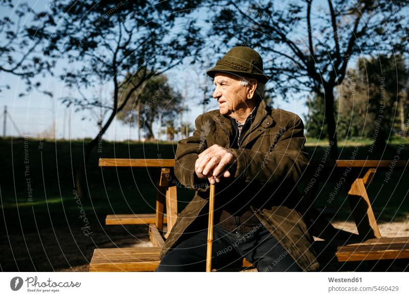 Alter Mann mit Stock auf einer Bank in einem Park sitzend Hüte Bänke Sitzbank Sitzbänke sitzt Pension pensioniert Pensionierung Rente erfahren Erfahrungen