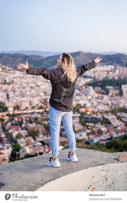 Rückansicht einer sorglosen jungen Frau, die bei Sonnenaufgang über der Stadt steht, Barcelona, Spanien Leute Menschen People Person Personen Europäisch