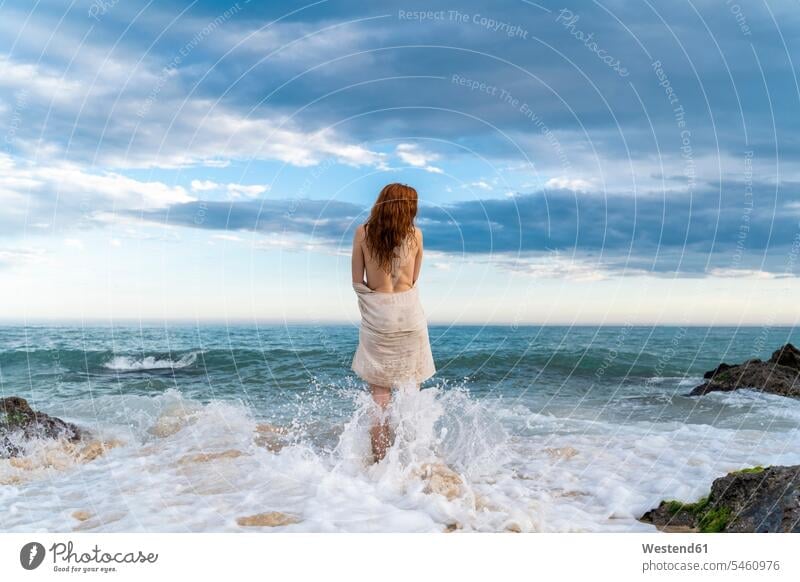 Rückenansicht einer rothaarigen, hemdlosen jungen Frau, die vor dem Meer steht Urlaub Ferien Brandung nackter Oberkörper freier Oberkörper genießen geniessen