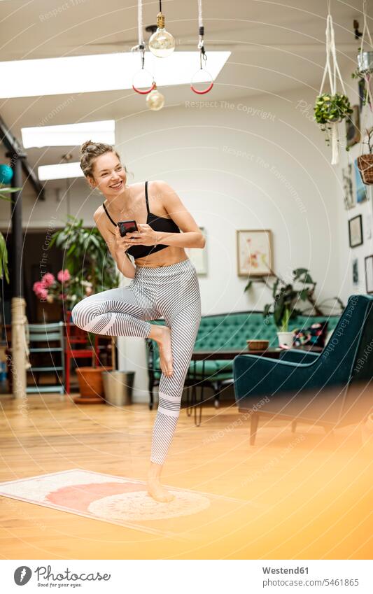 Junge Frau, die zu Hause Yoga praktiziert und ein Smartphone in der Hand hält Stuehle Stühle Telekommunikation telefonieren Handies Handys Mobiltelefon