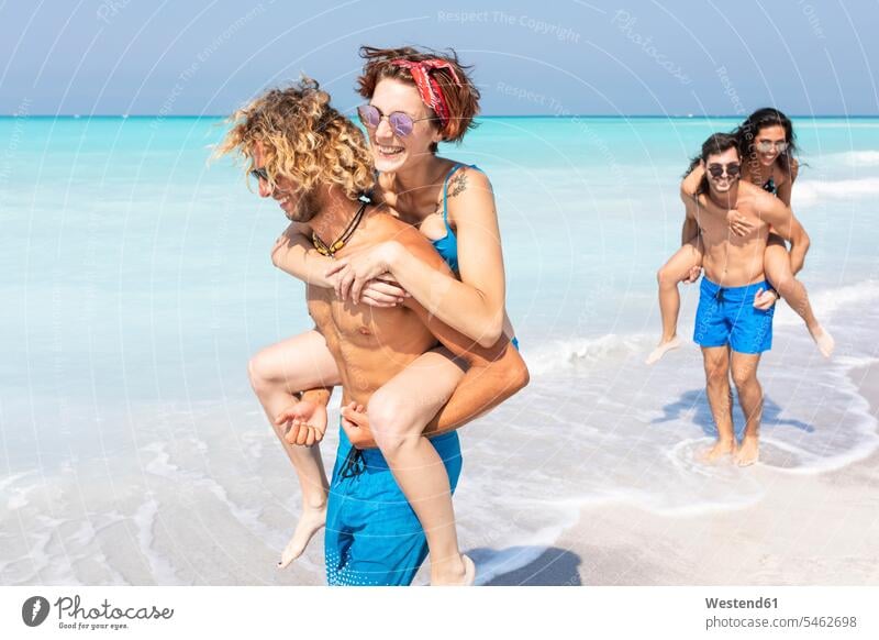 Freunde, die am Strand spazieren gehen und ihre Freundinnen Huckepack tragen transportieren Beach Straende Strände Beaches Meer Meere aktiv Spaß Spass Späße