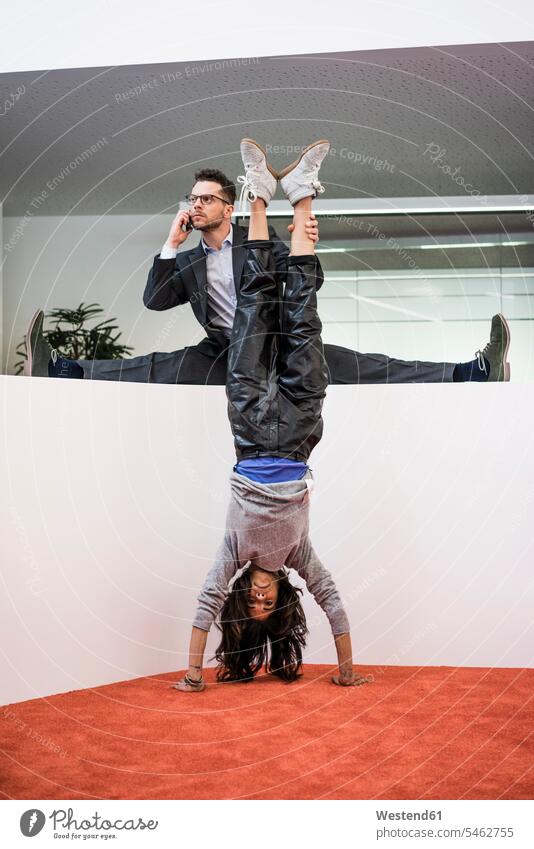 Geschäftsmann im Büro hält die Beine der Frau einen Handstand machen Leute Menschen People Person Personen Europäisch Kaukasier kaukasisch erwachsen Erwachsene