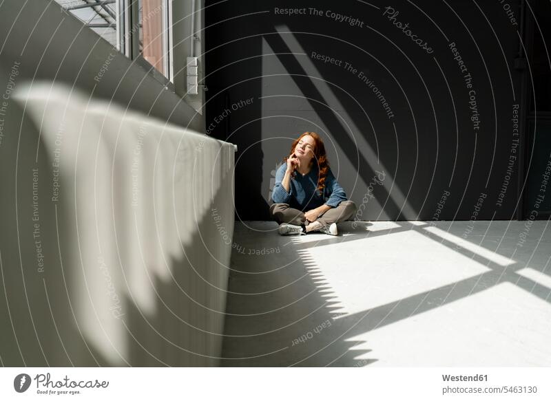 Rothaarige Frau sitzt auf dem Boden eines Dachbodens und genießt das Sonnenlicht Leute Menschen People Person Personen Europäisch Kaukasier kaukasisch 1 Ein