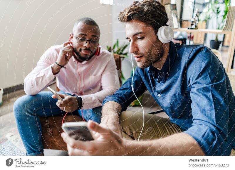 Junger Mann zeigt einem Kollegen, der in einem Loft sitzt, sein Handy Männer männlich Lofts Arbeitskollegen Mobiltelefon Handies Handys Mobiltelefone sitzen