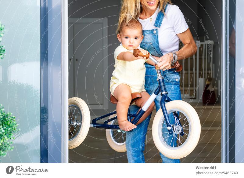 Mutter spielt mit ihrem Sohn, der zu Hause auf einem Dreirad sitzt Farbaufnahme Farbe Farbfoto Farbphoto Innenaufnahme Innenaufnahmen innen drinnen Tag