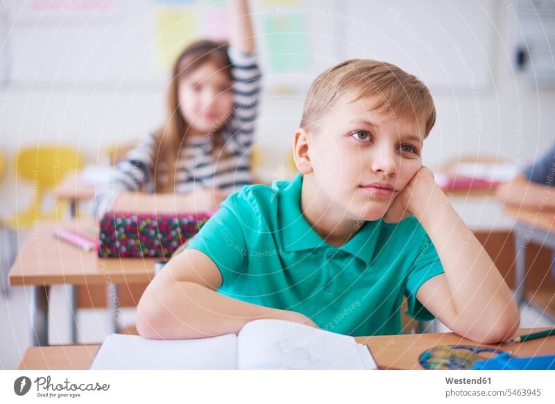 Gelangweilter Schuljunge in der Klasse mit einem Mädchen, das im Hintergrund die Hand hebt Langeweile langweilig gelangweilt Schule Schulen Schulklasse Schüler