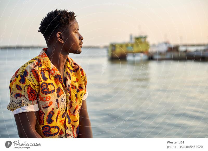 Am Meer stehender junger Mann, Porträt Leute Menschen People Person Personen Afrikanisch Afrikanische Abstammung dunkelhäutig Farbige Farbiger Schwarze 1 Ein