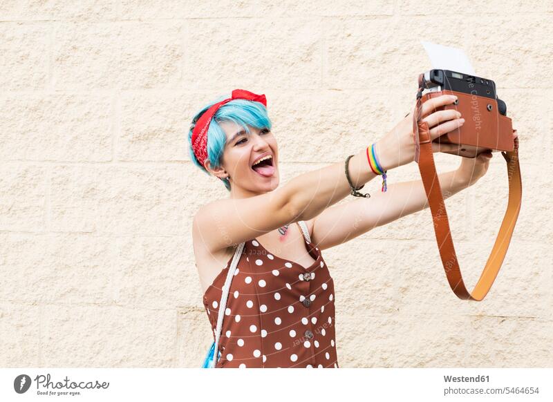 Porträt einer jungen Frau mit blau gefärbtem Haar, die ein Selfie mit einer Sofortbildkamera macht Foto Fotos Polaroid-Kamera Haare Portrait Porträts Portraits