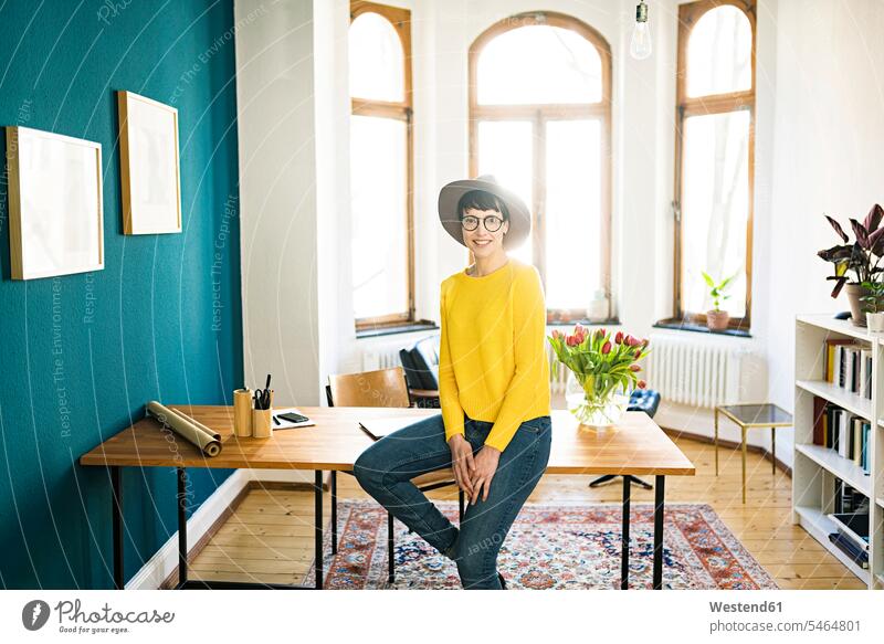 Porträt der lächelnden Geschäftsfrau im Home-Office sitzt auf dem Tisch arbeiten Arbeit Wohnung Mietwohnungen wohnen Zuhause zu Hause daheim sitzen sitzend