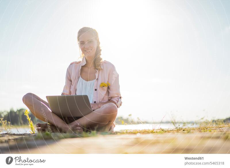 Porträt der lächelnden Frau sitzt am Flussufer im Sommer mit Laptop Portrait Porträts Portraits Fluesse Fluß Flüsse Sommerzeit sommerlich Notebook Laptops