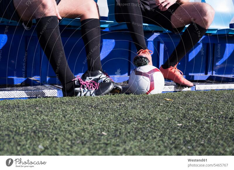 Beine von zwei Fußballspielern, die auf einer Bank am Fußballplatz sitzen Fussballplatz Fußballplätze Fussballplaetze Fussballspieler Fussballer Fußballer