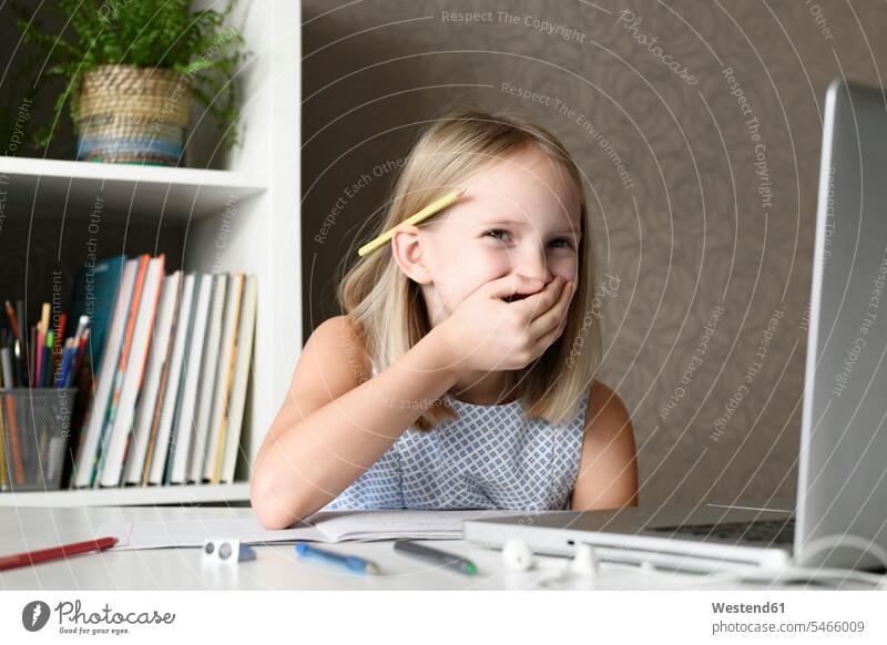 Lachendes Mädchen sitzt zu Hause mit Laptop am Tisch Tische Stifte Rechner Laptops Notebook Notebooks sitzend freuen Frohsinn Fröhlichkeit Heiterkeit Glück