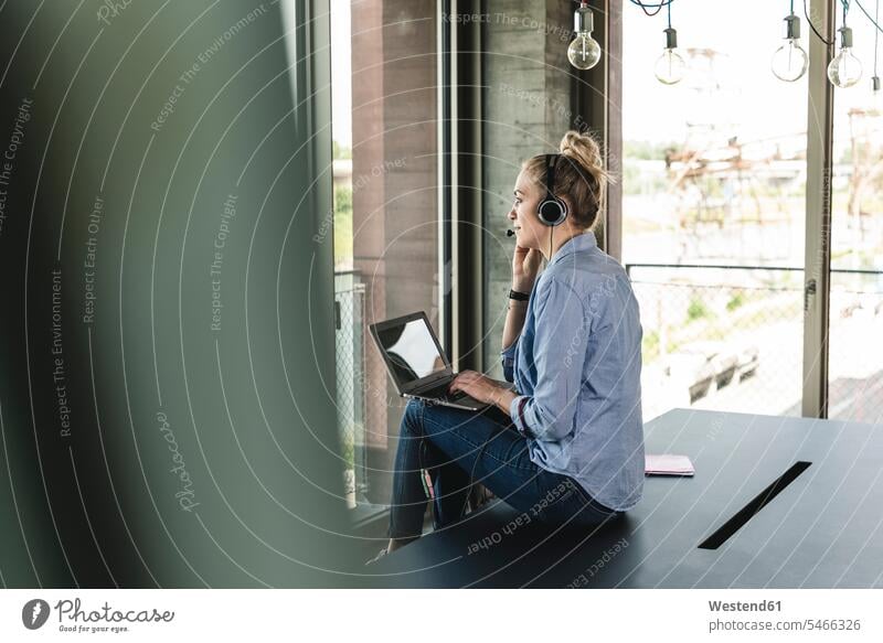 Junge Geschäftsfrau sitzt am Schreibtisch, telefoniert, benutzt Headset und Laptop Headsets Geschäftsfrauen Businesswomen Businessfrauen Businesswoman Anruf