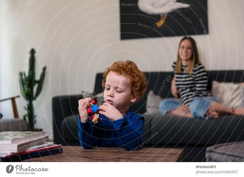 Mutter entspannt sich auf dem Sofa, während der Sohn zu Hause mit einem Spielzeugroboter auf dem Tisch spielt Farbaufnahme Farbe Farbfoto Farbphoto