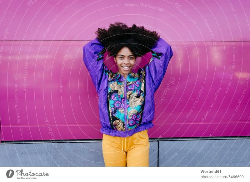 Lächelnde junge Frau spielt mit ihren Haaren, rosa Wand im Hintergrund Jacken freuen Glück glücklich sein glücklichsein zufrieden farbig mehrfarbig lilafarben