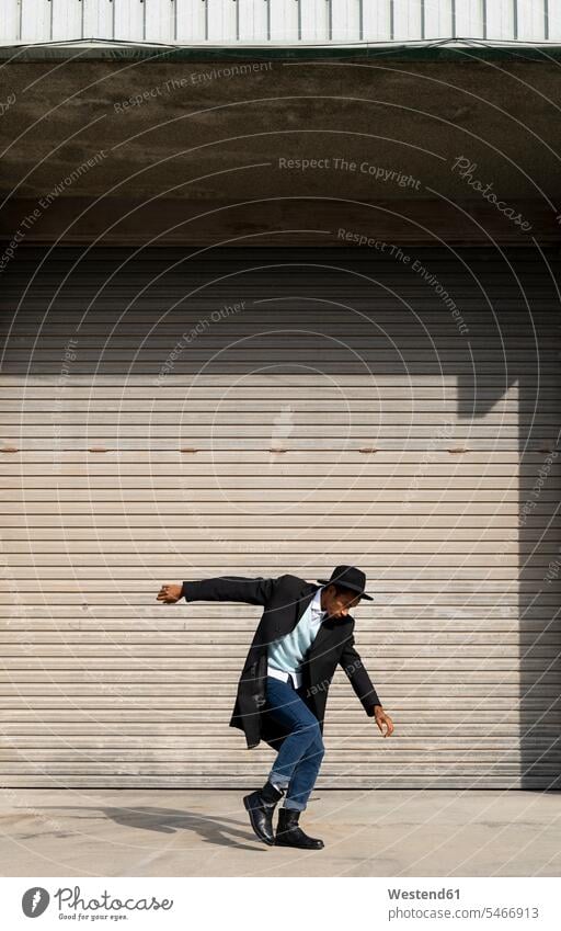 Glücklicher junger Mann tanzt gegen Rollladen Farbaufnahme Farbe Farbfoto Farbphoto Außenaufnahme außen draußen im Freien Tag Tageslichtaufnahme