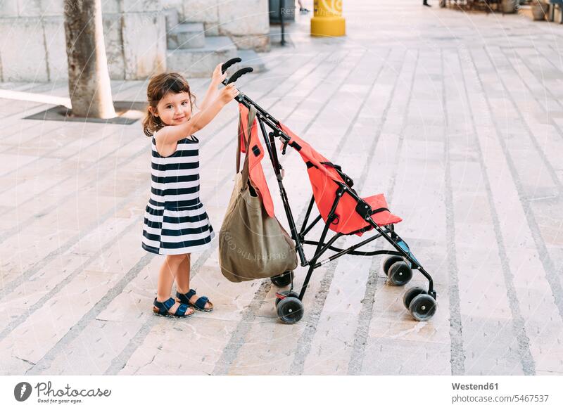 Porträt eines lächelnden kleinen Mädchens, das seinen Kinderwagen schiebt Leute Menschen People Person Personen Europäisch Kaukasier kaukasisch 1 Ein ein Mensch