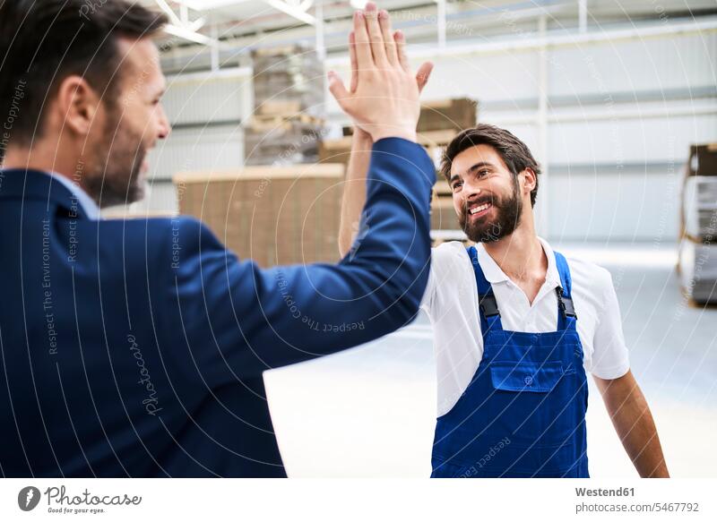 Glücklicher Geschäftsmann und Arbeiter High Fiving in einer Fabrik Job Berufe Berufstätigkeit Beschäftigung Jobs Boss Bosse Chefs Vorgesetzte Vorgesetzter