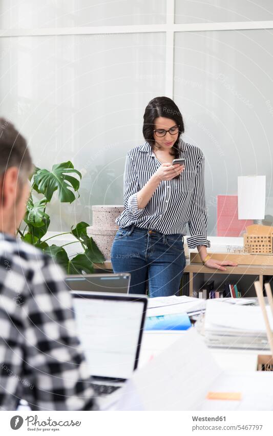 Porträt einer Frau mit einem Kollegen, der im Büro ein Mobiltelefon benutzt Portrait Porträts Portraits Arbeitskollegen Office Büros Handy Handies Handys