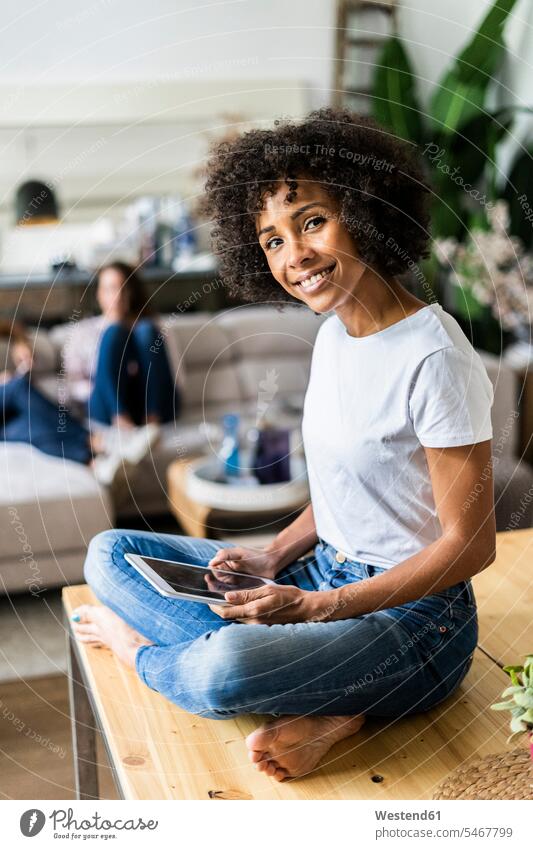 Porträt einer lächelnden Frau mit Tablet auf dem Tisch zu Hause mit Freunden im Hintergrund Portrait Porträts Portraits Tische Freundinnen Zuhause daheim sitzen