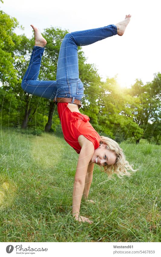 Porträt einer glücklichen blonden Frau beim Handstand auf einer Wiese weiblich Frauen Portrait Porträts Portraits Handstaende Handstände Wiesen blonde Haare