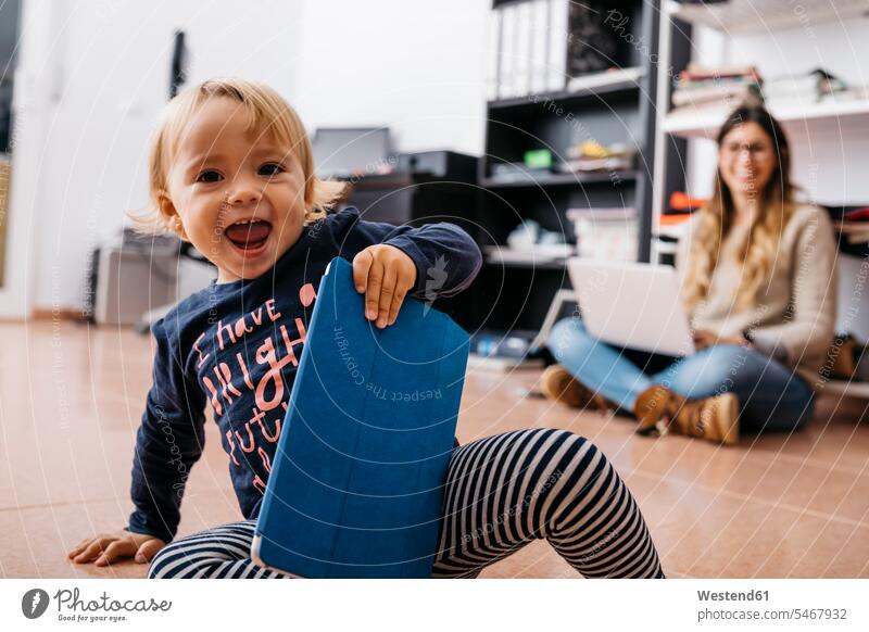 Glückliches kleines Mädchen sitzt auf dem Boden zu Hause mit Tablet und Mutter im Hintergrund Mami Mutti Mütter Mama Böden Boeden Tablet Computer Tablet-PC