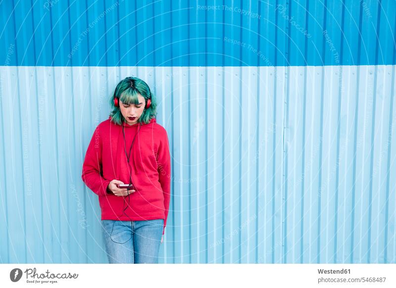 Junge Frau mit blau gefärbten Haaren hört Musik mit Kopfhörern beim Blick auf Smartphone blaue blauer blaues Portrait Porträts Portraits weiblich Frauen iPhone