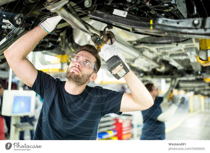 Zwei Kollegen arbeiten am Autounterboden in einer modernen Fabrik Arbeitskollege Arbeitskollegen Job Berufe Berufstätigkeit Beschäftigung Jobs Arbeiter T-Shirts