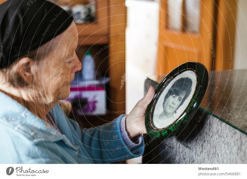 Ältere Frau schaut auf alten Bilderrahmen zu Hause Farbaufnahme Farbe Farbfoto Farbphoto Innenaufnahme Innenaufnahmen innen drinnen Tag Tageslichtaufnahme