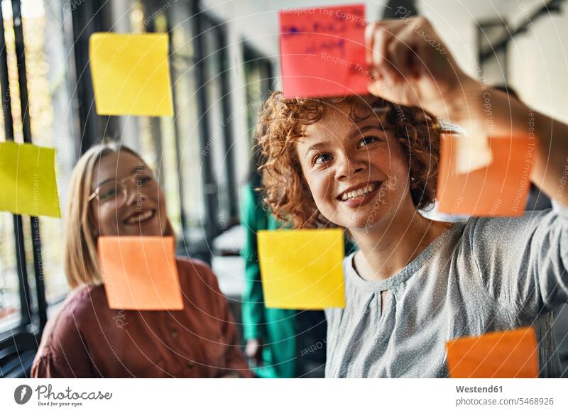 Glückliche Kollegen mit Haftnotizen an der Glasscheibe im Büro Arbeitskollege Arbeitskollegen Job Berufe Berufstätigkeit Beschäftigung Jobs geschäftlich