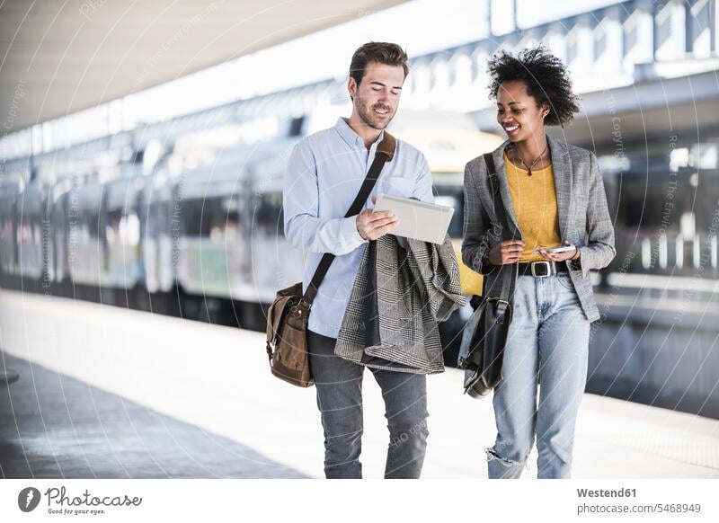 Junger Geschäftsmann und Geschäftsfrau benutzen gemeinsam Tabletten am Bahnhof Leute Menschen People Person Personen Afrikanisch Afrikanische Abstammung