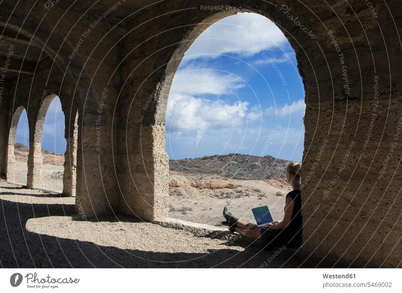 Spanien, Teneriffa, Abades, Sanatorio de Abona, Frau sitzt in Geisterstadt Gebäude mit Laptop weiblich Frauen Notebook Laptops Notebooks Fenster Bogen Gewölbe