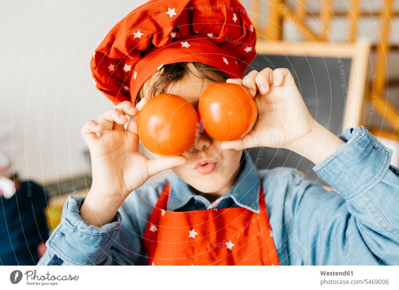 Verspielter Junge, der in der Küche seine Augen mit Tomaten bedeckt Gastronomie Koeche Kuechenchef Kuechenchefs Köche Küchenchef Küchenchefs freuen Frohsinn