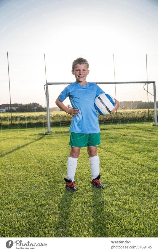 Porträt eines lächelnden jungen Fussballspielers, der den Ball auf dem Fussballplatz hält Fußballspieler Fussballer Fußballer Fußballplatz Fußballplätze