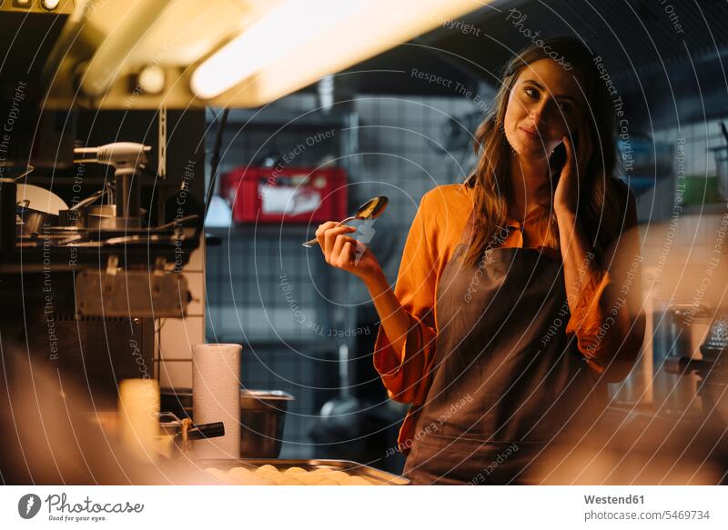 Junge Frau spricht mit dem Handy in der Restaurantküche Deutschland Selbstständigkeit Selbständigkeit Freiberufler zubereiten kochen Essen zubereiten Smartphone