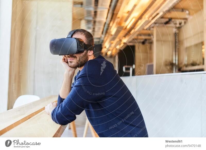 Junger Mann mit VR-Brille in modernem Büro aufstützen aufgestuetzt aufgestützt 3D dreidimensional 3-D 3-d Office Büros Virtual Reality Virtuelle Realität