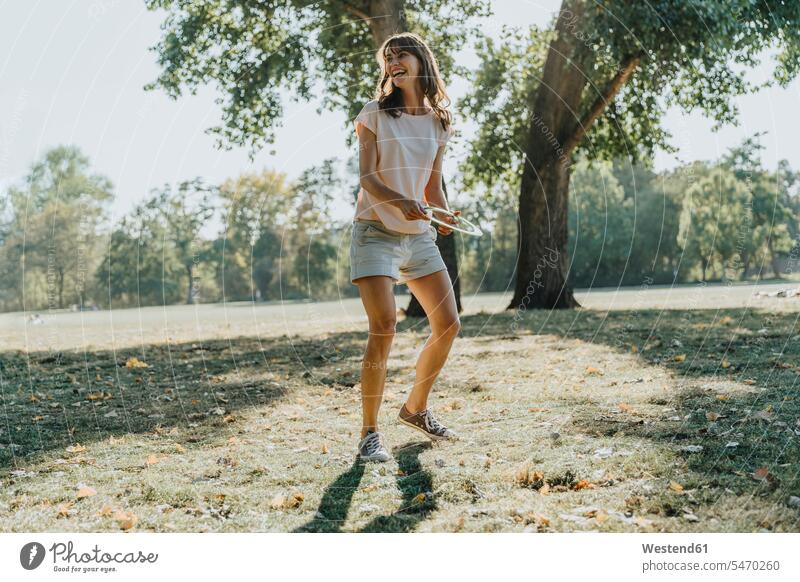 Reife Frau wirft Frisbee-Ring, während sie an einem sonnigen Tag im öffentlichen Park steht Farbaufnahme Farbe Farbfoto Farbphoto Außenaufnahme außen draußen