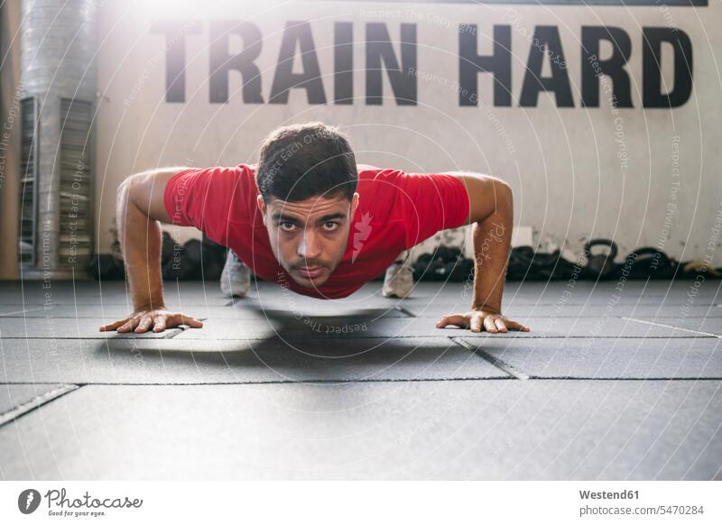 Selbstbewusster männlicher Athlet beim Üben von Liegestützen auf dem Boden im Fitnessstudio Farbaufnahme Farbe Farbfoto Farbphoto Innenaufnahme Innenaufnahmen